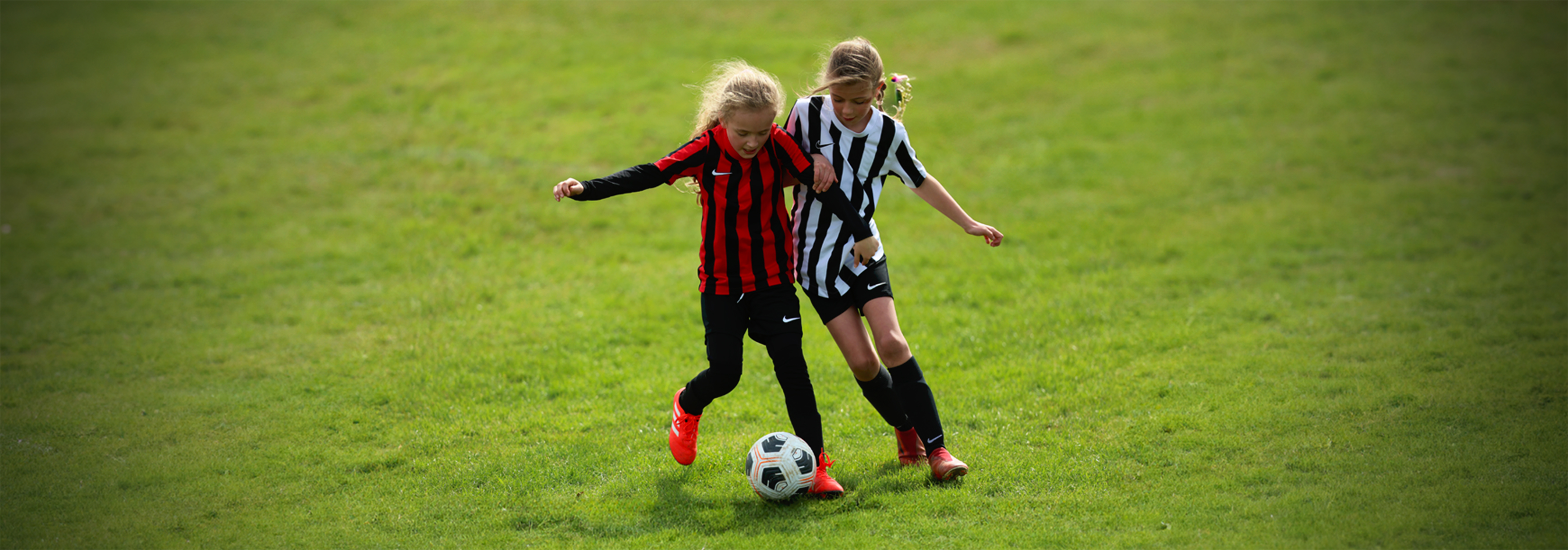 One player runs with the ball while another, close behind her on the left, puts her under pressure as she looks to make a tackle.