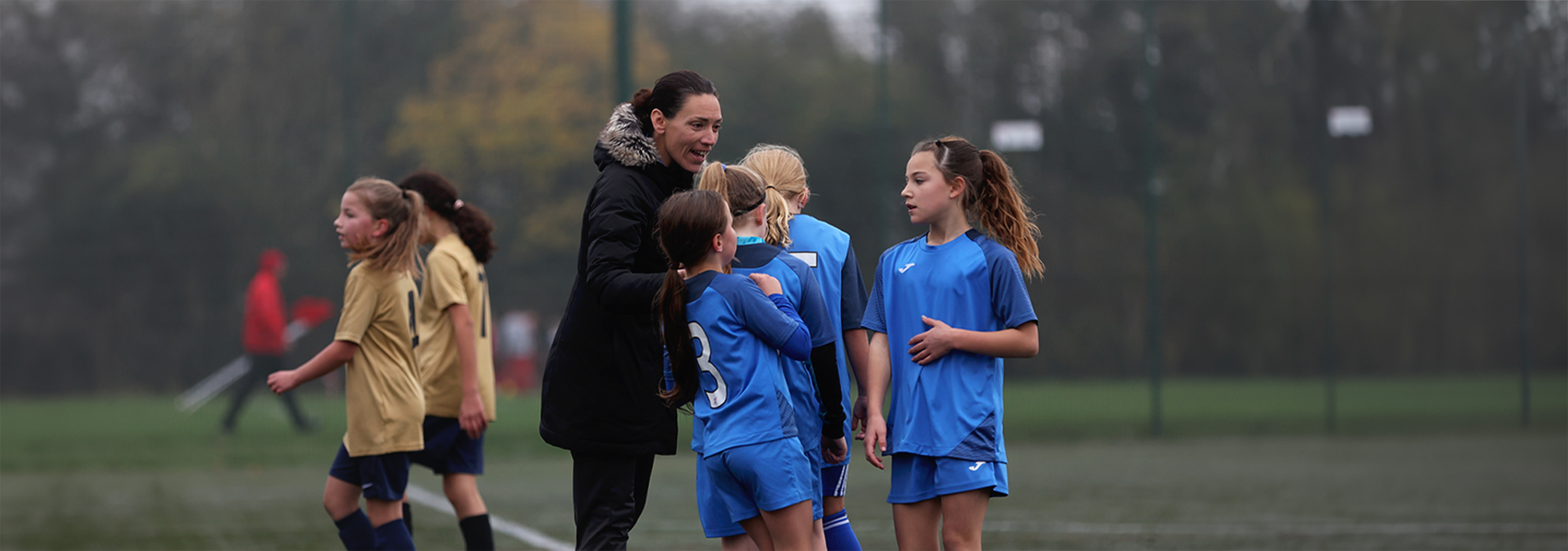 A coach talks to a small group of her players at the side of the pitch during matchday.