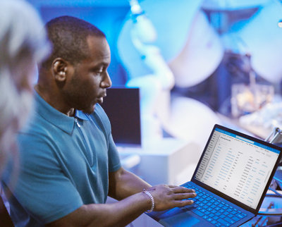 Man reviewing data on a laptop in a busy office setting with colleagues surrounding him.