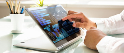 Person analyzing financial data on a tablet screen with interactive charts and graphs, in a bright office setting.