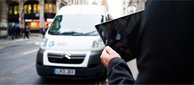Um homem segurando um tablet em frente a uma van.