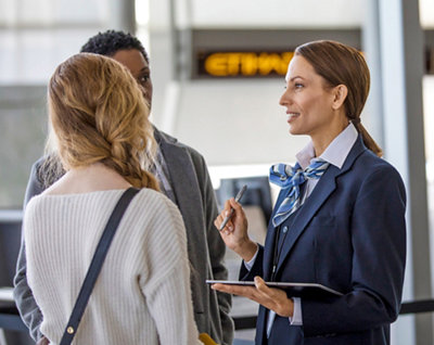 Uma mulher usando um terno falando com um grupo de pessoas em um aeroporto.