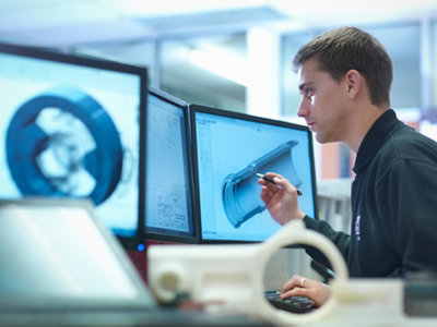 A man examines a 3d model on a computer screen in a high-tech workspace, holding a pen and focusing intently.