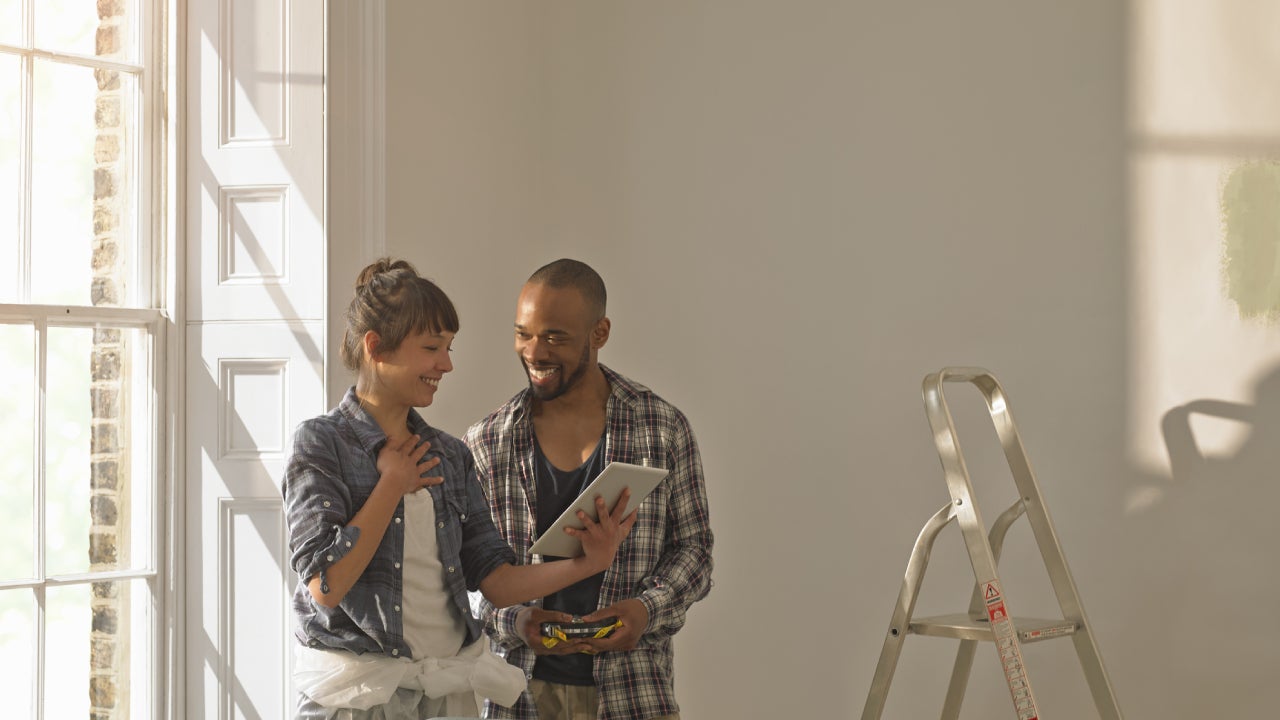 A young couple is standing together in their unfinished living room.