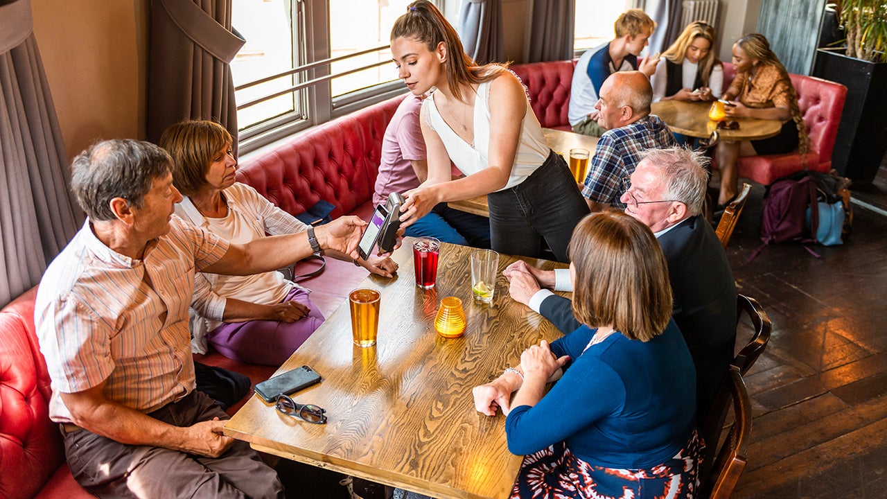 A man using his phone to pay for drinks at the table in a British pub.