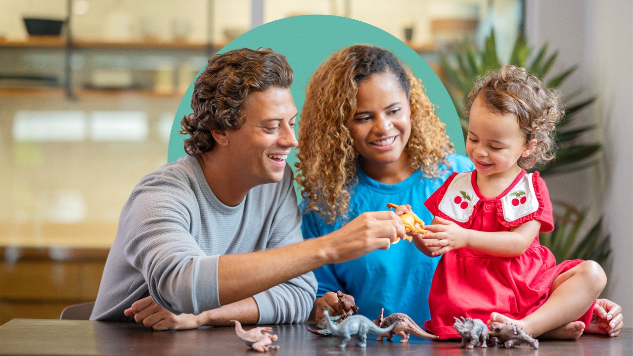 Mixed-race family playing with toy dinosaurs with their child.