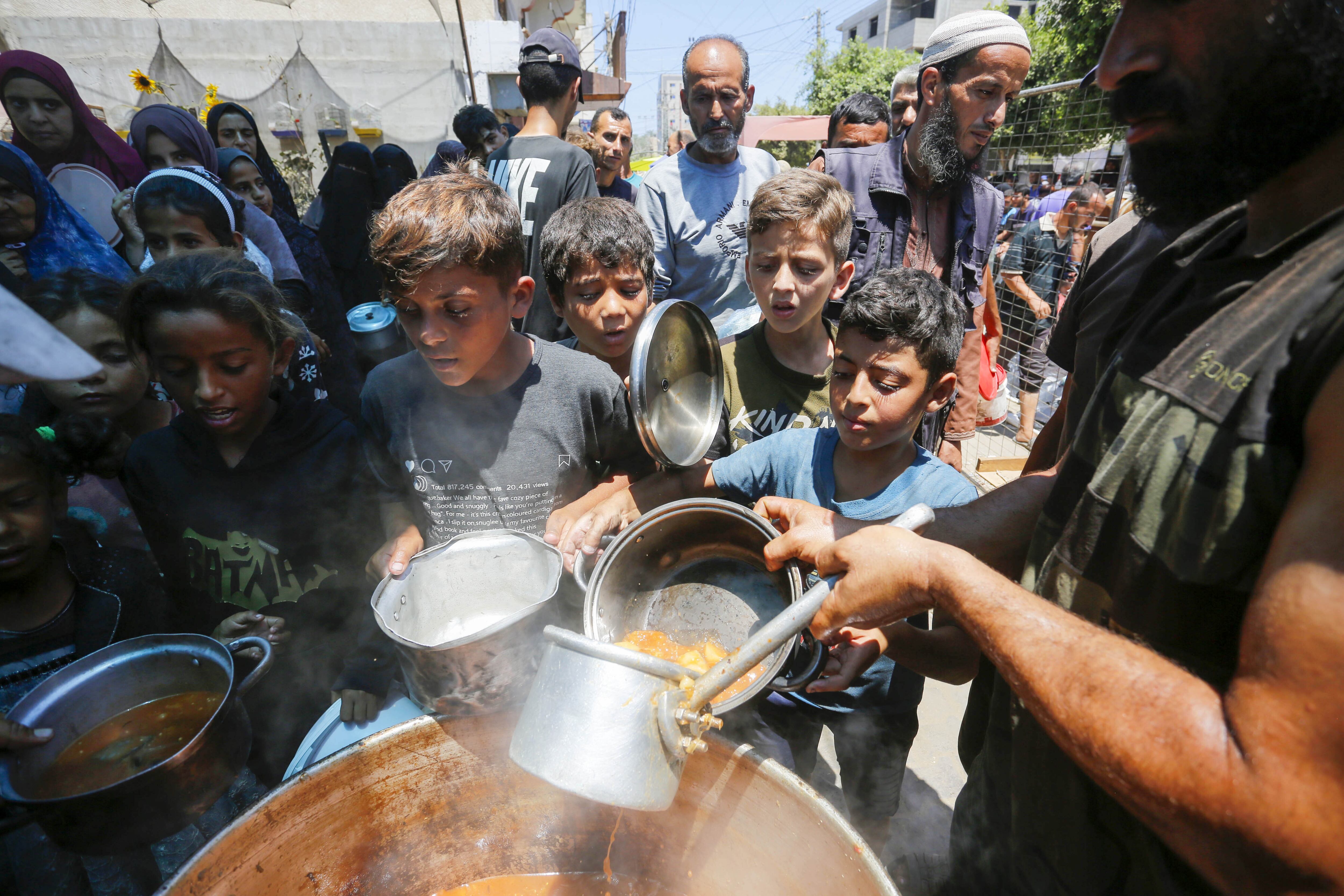 Varios niños palestinos desplazados reciben comida caliente distribuida por una ONG, este miércoles en Deir Al-Balah en Gaza.