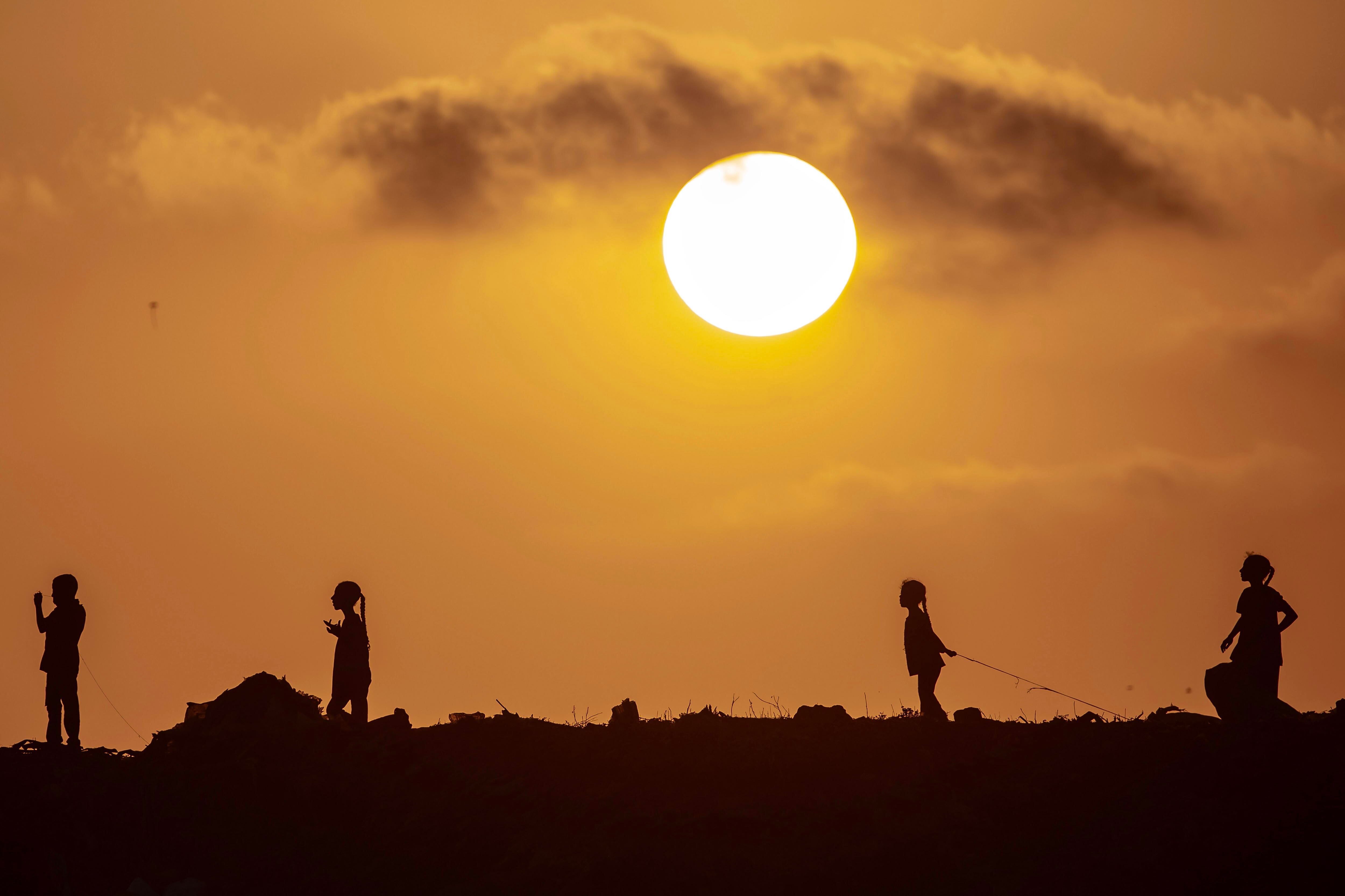 Niños palestinos al atardecer en el campo de refugiados de Jan Yunis, subidos a una colina de basura donde buscan material para hacer fuego debido a la escasez de gas, este domingo al sur de la franja de Gaza.