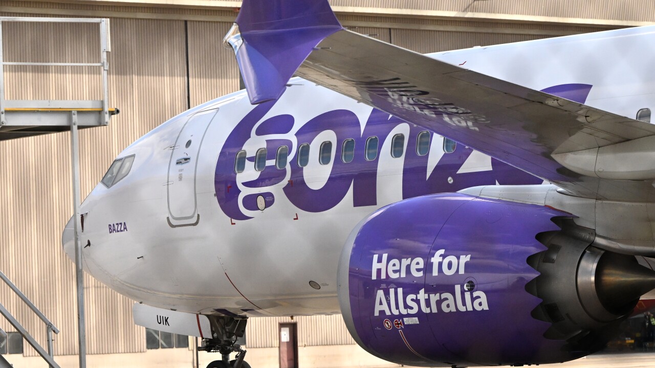 A plane emblazoned with Bonza's trademark purple and white colours sits motionless beside a hangar. 