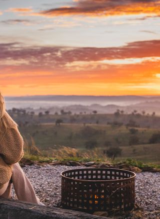 Woman enjoying the firepit while watching the sunrise from the Uralla Tent at Sierra Escape, Piambong