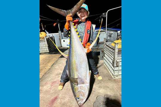 Fishery observer holding a large tuna by the tail longer than her.