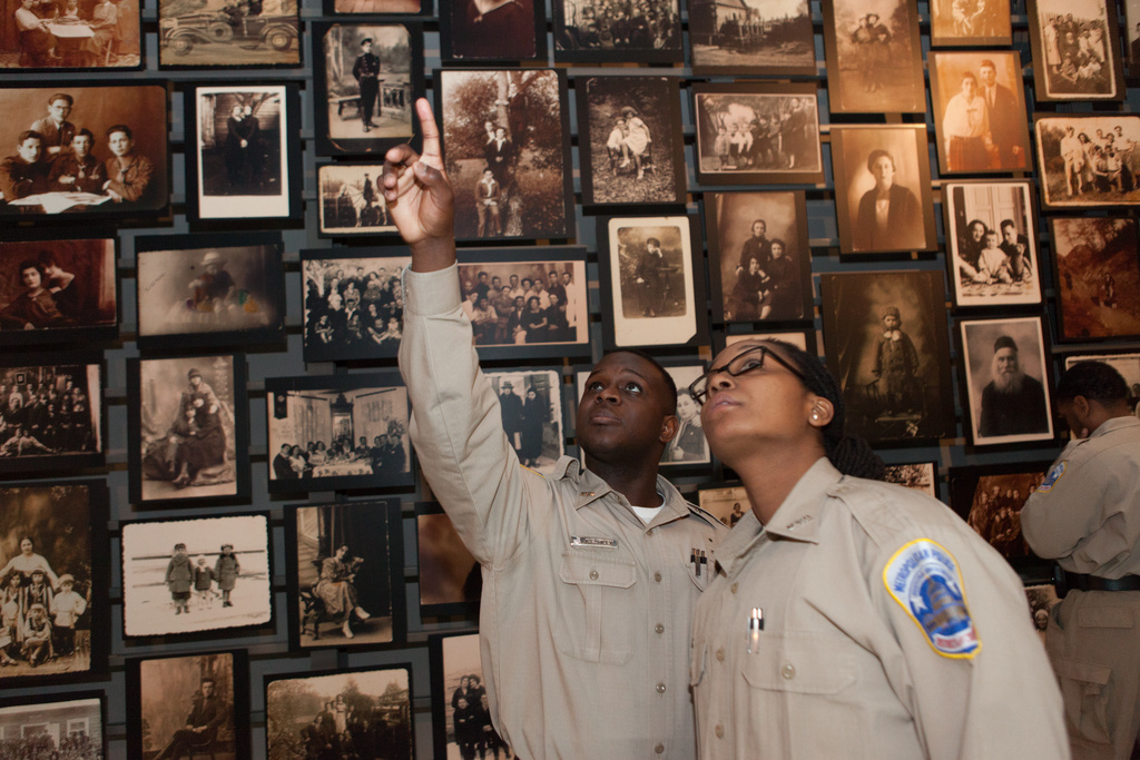 Two uniformed Museum visitors point up to a photo in the Tower of Faces