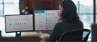 A woman is sitting at a desk with two monitors.