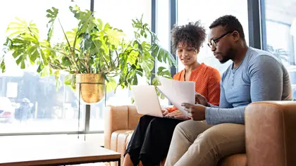 Couple sitting on the couch, reviewing paperwork, and using laptop together