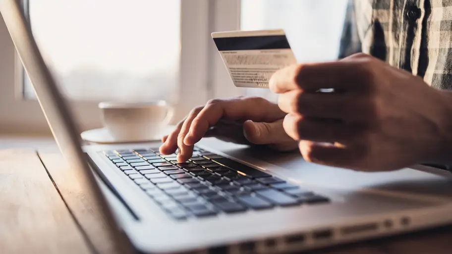 close up of a person typing while holding a card in front of a laptop