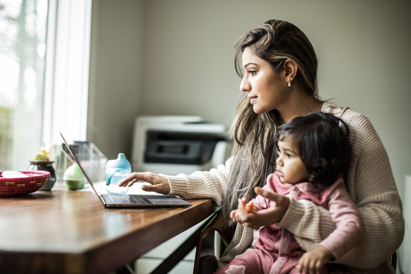 A working mother multitasks with her infant daughter in her home office