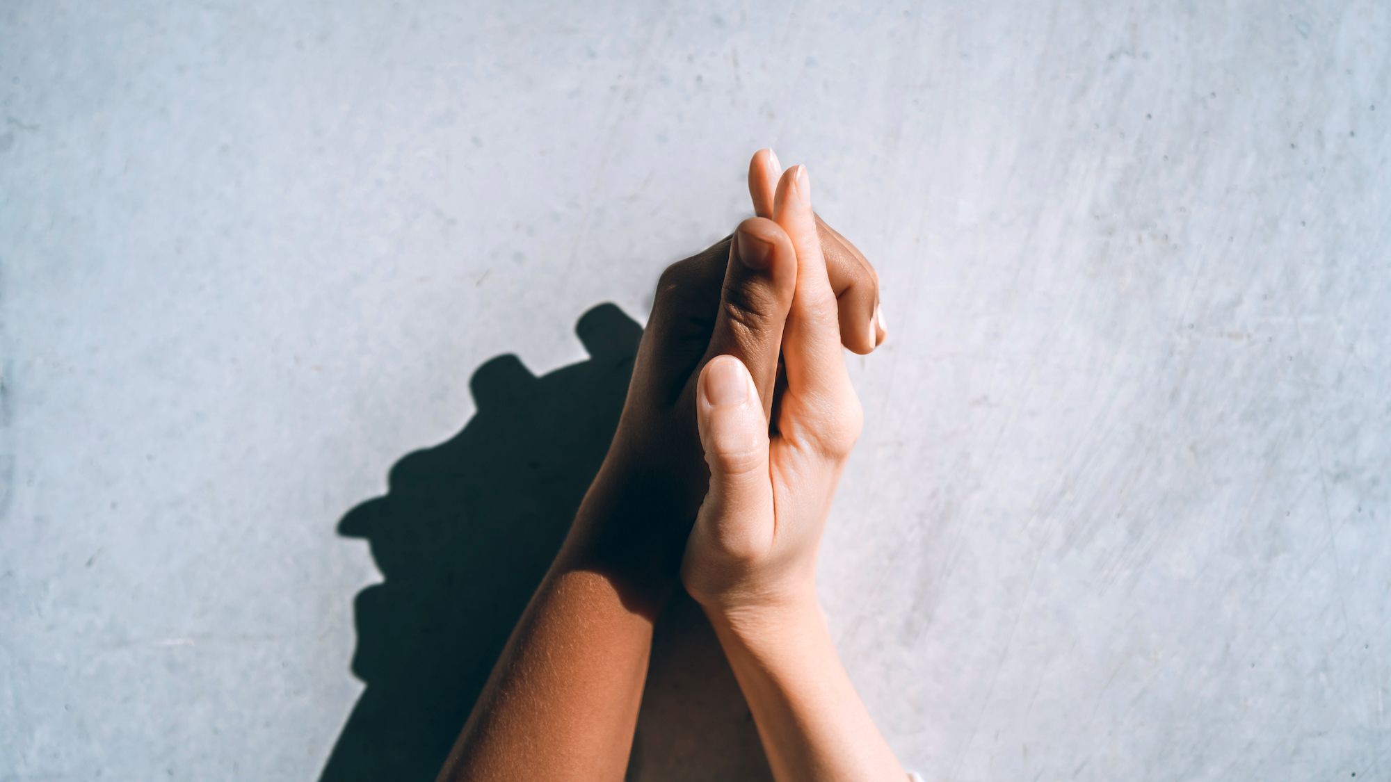 Two multiracial women holding hands against a concrete gray wall, white and black skin tones. Symbol of international couples. Gender, age, and nationality equality, individuality and diversity concepts. LGBT relationships