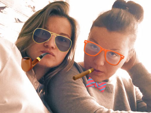 Photo of two young girls having fun decorated with zany stickers: sigars, sunglasses, etc.