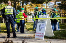 Emergency responders standing outside by yellow tape next to a sign that says "UK Police Department, Training in Progress"