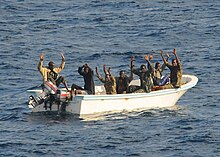 Seven men in a small motor skiff with their hands raised