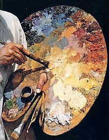 Moški prst zataknjen skozi luknjo v veliki leseni paleti. Ena njegovih rok potaplja čopič v barvo, druga pa drži rezervne čopiče.