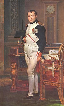 Full length portrait of a man in his forties, in high-ranking dress white and dark blue military uniform. He stands amid rich 18th-century furniture laden with papers, and gazes at the viewer. His haer is Brutus style, cropped close but with a short fringe in front, and his right hand is tucked in his waistcoat.
