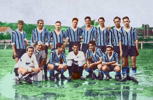 Foto do primeiro time gremista, em dezembro de 1903. 23 homens de braços cruzados com camisetas de longas longas em listras nas cores marrom e azul, gravatas brancas e calças azul escuro. 11 deles estão em pé, seis ajoelhados e e seis sentados no chão.