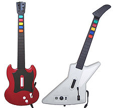 A photograph of two guitar-shaped video game controllers side by side, the left one red and the right one white all on a solid, white background