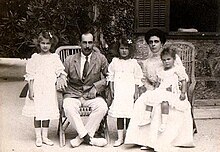 Photographie en noir et blanc d'un couple assis sur une terrasse et entourée de trois petites filles.