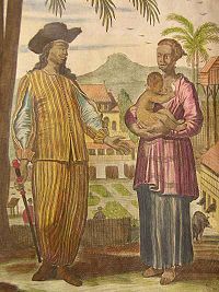 A colorized engraving of a family. The man has a hat, long hair and a stick. The woman holds a baby. In the background there are buildings and palm trees.