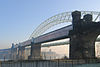 A bridge consisting of four girders on sandstone piers crossing the River Mersey seen on a frosty morning; beyond the railway bridge is the arch of the road bridge and under the arches is a church