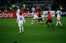 Several men in white shirts stand around a man in a blue-and-red shirt who is falling to the ground.