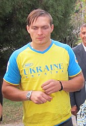 Photographie d'un homme debout habillé d'un T-shirt bleu et jaune, regardant vers le bas.