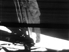 Poslední krok astronauta ve skafandru sestupujícího po žebříku na boku lunárního modulu