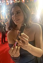 A woman with dark brown hair wearing a blue dress holding a phone