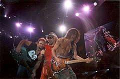 Trzech muzyków z gitarami rockowymi na scenie w trakcie koncertu.