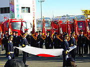 Tokyo'daki bir tören sırasında ulusal bayrak taşıyan itfaiyeciler