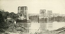 black and white photograph of burned-out bridge pillars in river