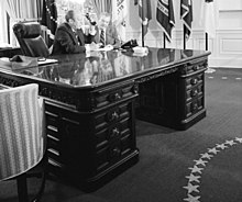 Gerald Ford sitting at a large mahogany desk in the Oval Office