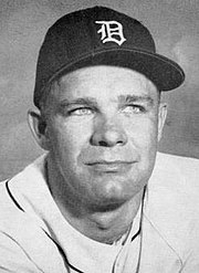 A man in a white baseball jersey and dark cap