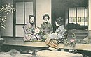 נשים יפניות לבושות בקימונו ויושבים בחזית בית יפני מסורתי. גלויה משנת 1900.