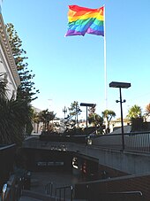 Photographie couleur d'un grand drapeau arc-en-ciel surplombant un espace en contrebas.