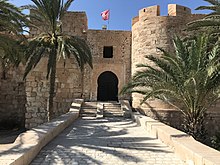 Façade du fort Borj El Kebir de Houmt Souk, partiellement masquée par des palmiers.