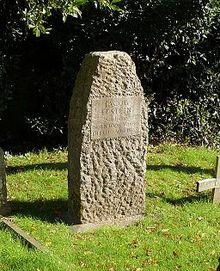 A narrow granite headstone with rough surface finish in a grassy cemetery