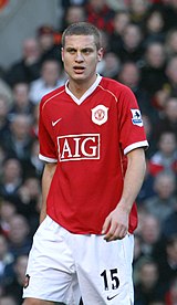 Nemanja Vidić, wearing a red Manchester United jersey with the AIG sponsor logo at the front centre and shorts with a number 15 and Nike logo on the left-leg side, looks forward with his mouth partly opened.