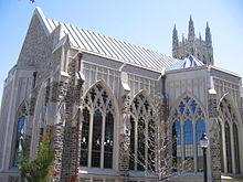 Cathedral-sized arched and intricate windows on chapel are displayed prominently in the foreground with larger soaring chapel peaking out at the top