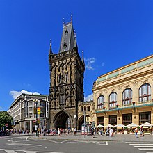 Une vue de la ville : à gauche, un bâtiment gris moderne ; au centre, une tour gothique, noire ; à droite, un bâtiment art nouveau, de couleur claire.