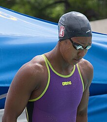 Lia Neal kurz vor dem Start. Sie trägt einen lila Badeanzug und eine Schwimmbrille. Auf der schwarzen Bademütze ist ein weißer Nadelbaum auf kardinalrotem S zu erkennen, das Zeichen der Stanford Cardinals.