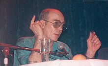 Photo of Hunter S Thompson with sunglasses speaking into a microphone