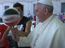 An athlete helps Pope Francis to spin a basketball on a pencil